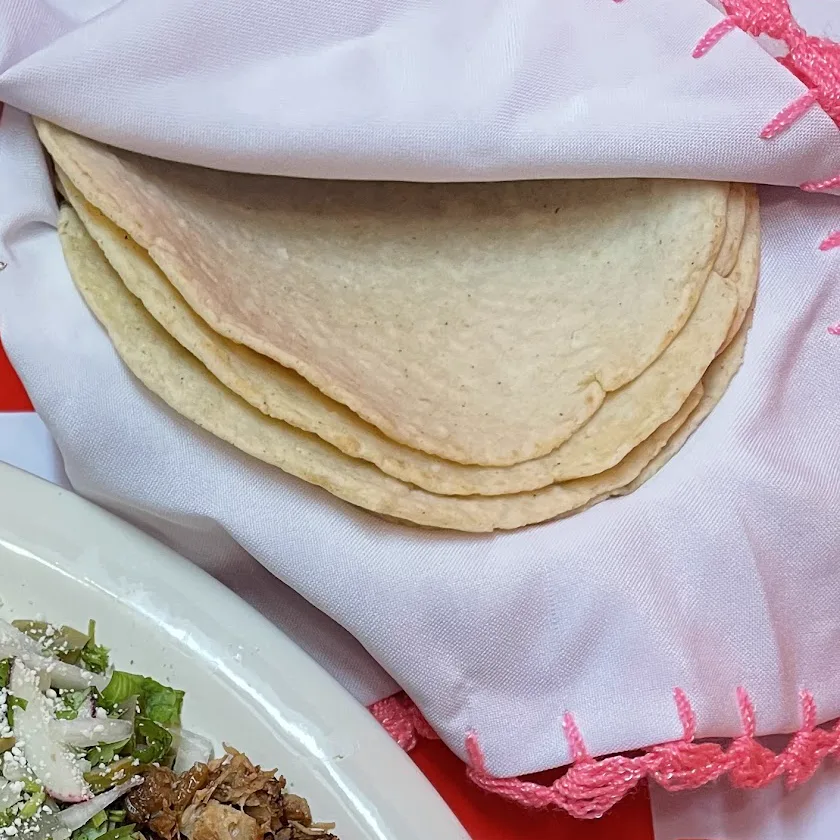 A stack of tortillas folded in a white cloth with pink embroidery