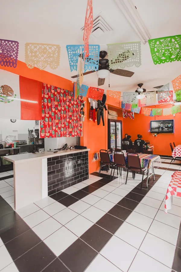 The dining room: orange walls, papel picado banners overhead, checkered tablecloths and a black and white tiled floor