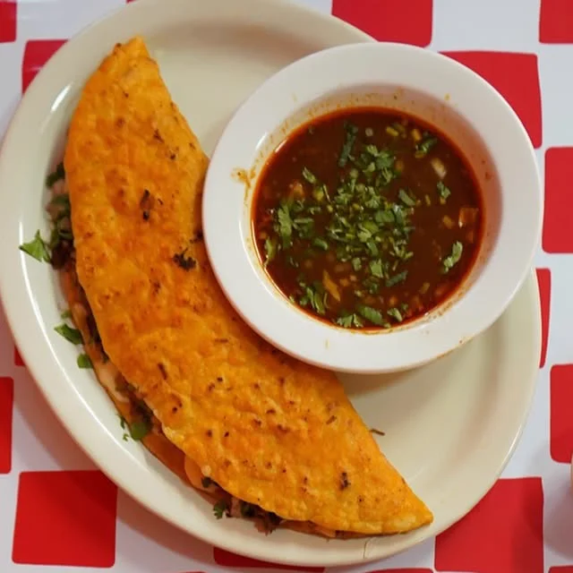 A birria quesadilla with a cup of consomé