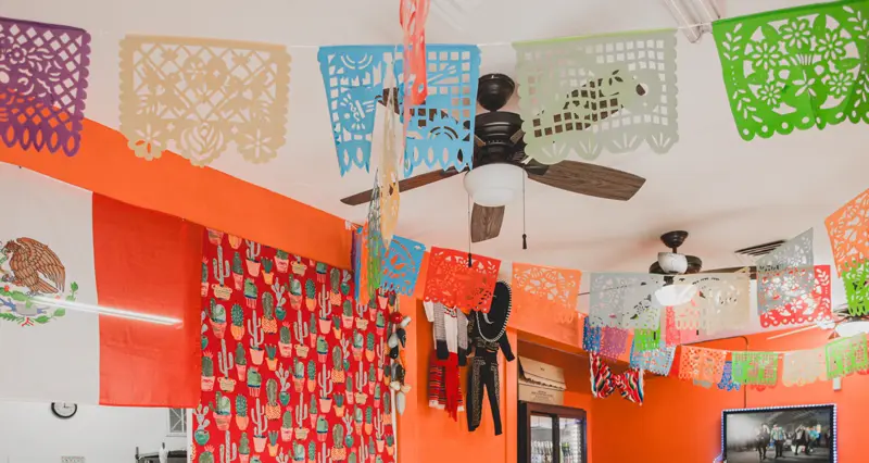 The dining room: orange walls, a Mexican flag and papel picado banners strung across the ceiling